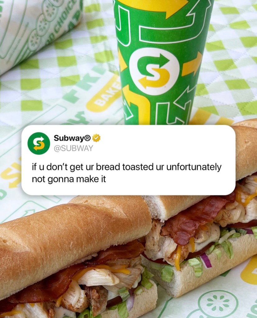 A close-up of two Subway sandwiches with layers of meat, lettuce, and bacon, accompanied by a branded drink cup and a colorful sandwich wrapper.